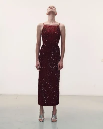 Model standing straight with head tilted back wearing a dark red embellished dress and silver heels on plain white backdrop