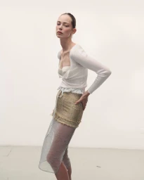 Model wearing a white top and textured skirt against a plain studio background for Des Phemmes spring/summer 2027.
