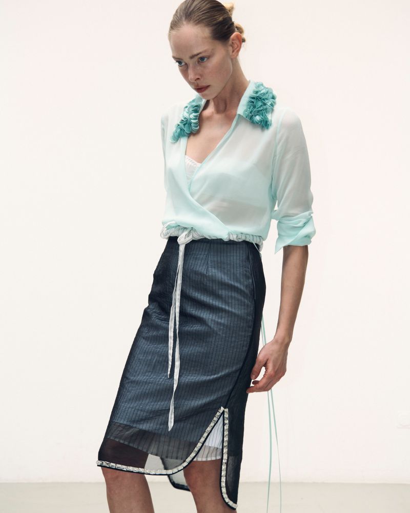 Model in mint green blouse with ruffled collar and dark pinstriped midi skirt against a plain white studio background.