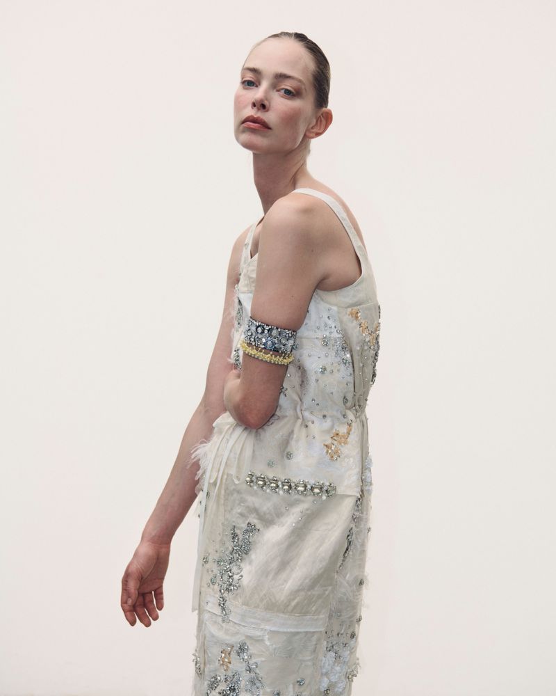 Model wearing embellished white dress with arm cuff against white background for Des Phemmes Spring/Summer 2027.