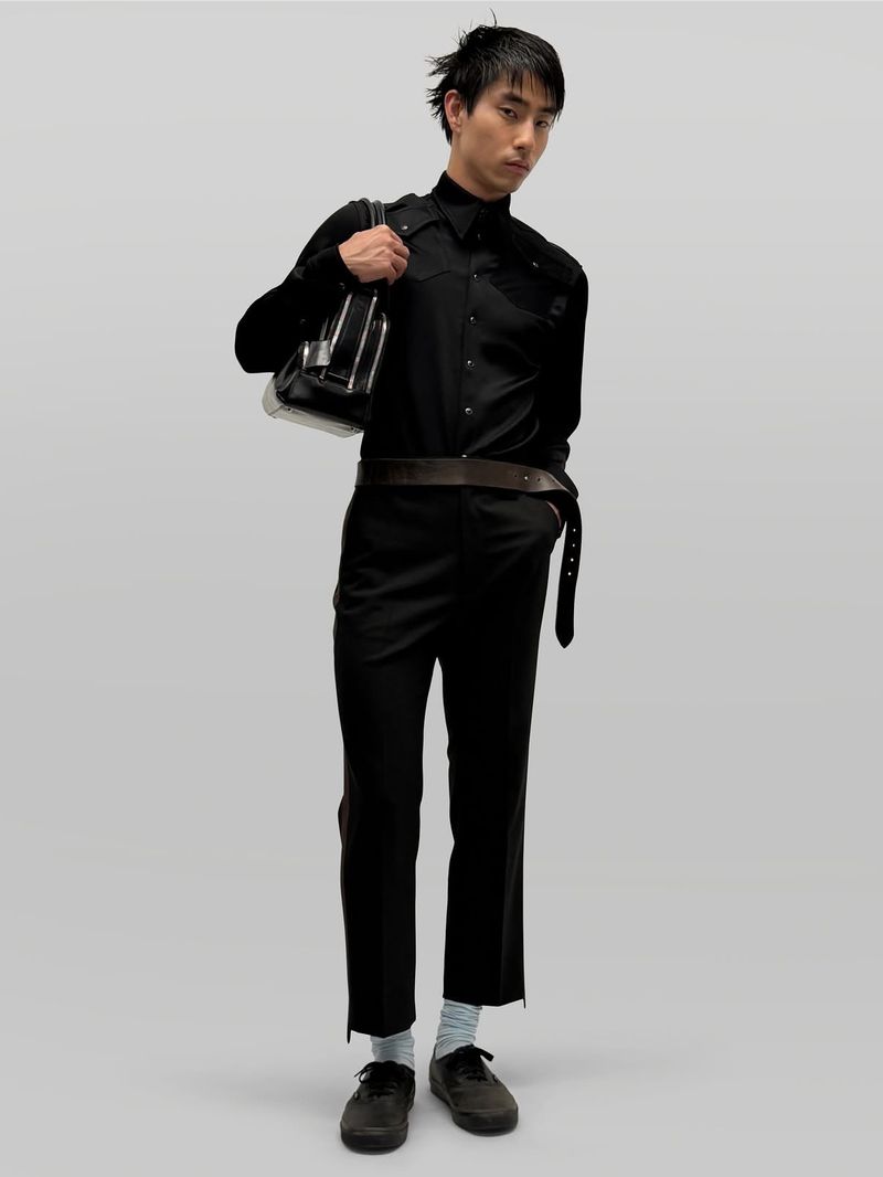 Model in all-black attire holding a structured handbag against a plain grey backdrop