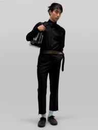 Model in all-black attire holding a structured handbag against a plain grey backdrop