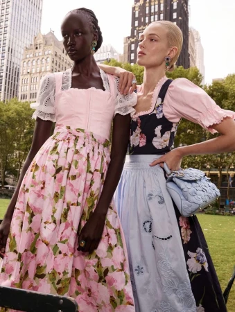 Two female models in floral dirndl dresses outdoors with city buildings in the background for Oscar de la Renta
