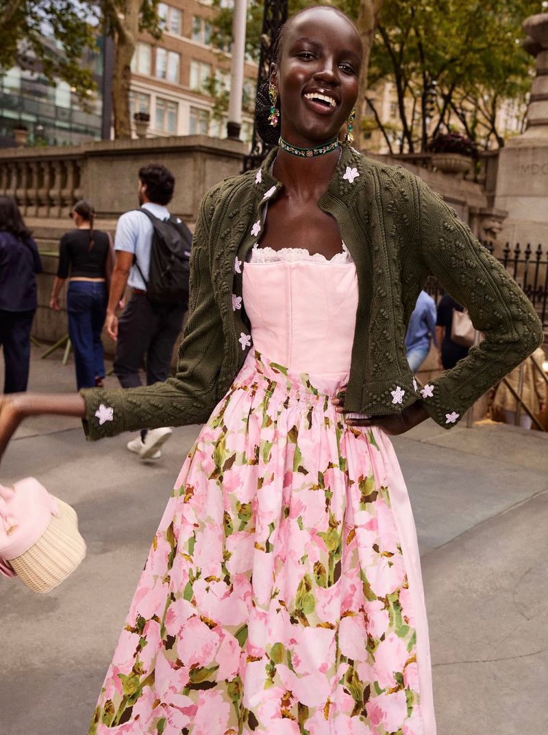 Model wearing a pink floral dress and olive cardigan on an outdoor city street for Oscar de la Renta.