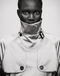 Portrait of a model wearing a high-collared trench coat against a plain light background