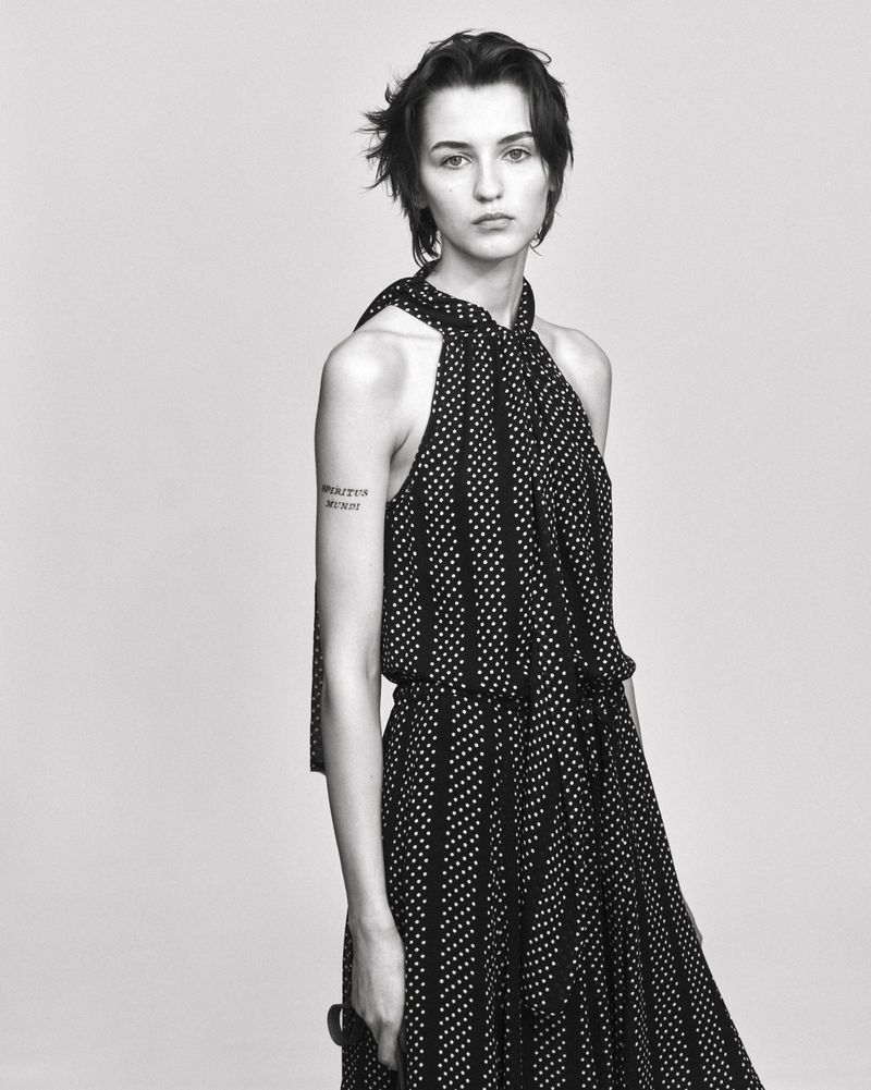 Model in a black and white patterned halter dress standing against a light grey studio background.