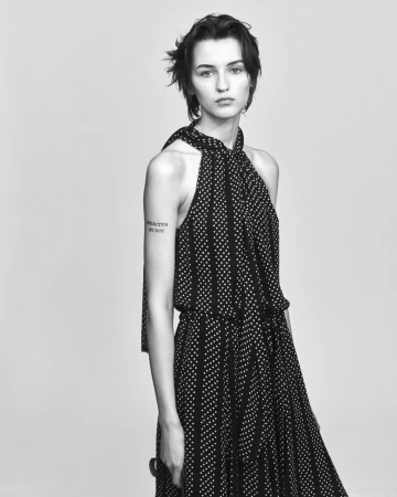 Model in a black and white patterned halter dress standing against a light grey studio background.