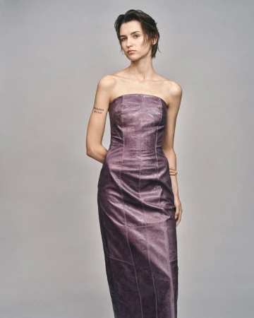Model with short dark hair wearing a strapless purple midi dress against a plain grey studio backdrop