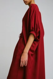Model wearing a loose red dress with gathered sleeves against a neutral grey studio background