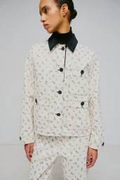 Model wearing a cream floral print jacket and matching trousers with a dark collar against a plain studio background.