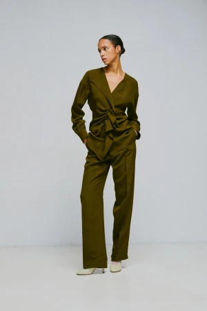 Model wearing an olive green wrap blouse and matching trousers against a light grey studio backdrop.