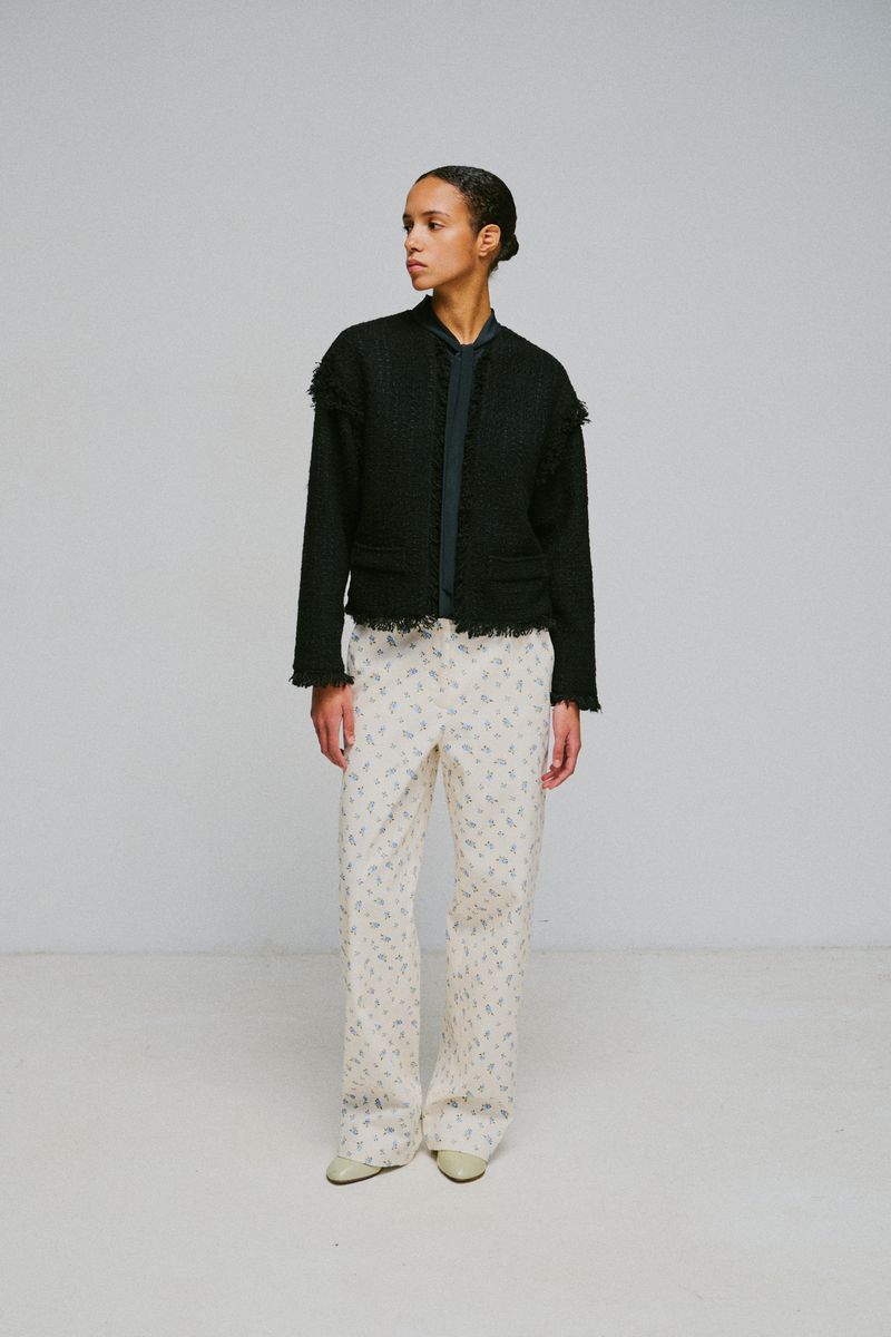 Model standing against a grey studio backdrop wearing a dark tweed jacket and patterned trousers