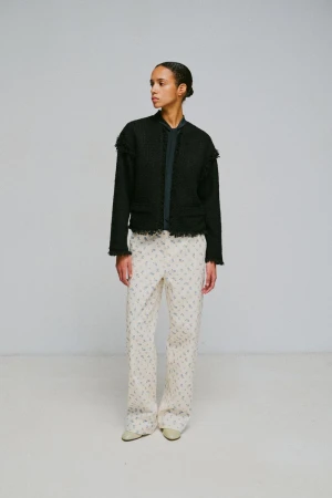 Model standing against a grey studio backdrop wearing a dark tweed jacket and patterned trousers