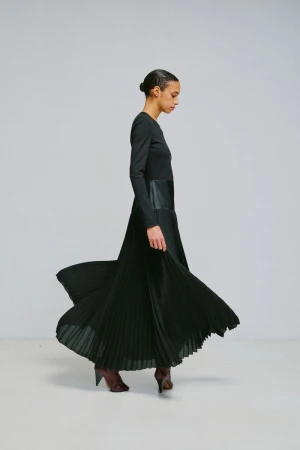 Model in a long black pleated dress spinning against a plain light grey studio background