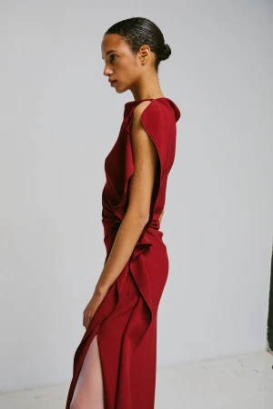 Profile view of a model in a red sleeveless dress with ruffled detailing against a white studio background.