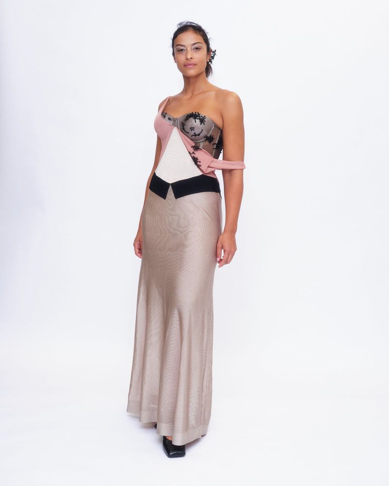 Model standing against a white seamless backdrop wearing a strapless gown with a structured bodice and long skirt.