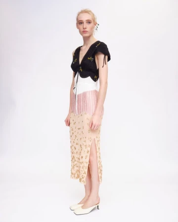Model wearing a black and beige pleated dress with floral details standing against a plain white background