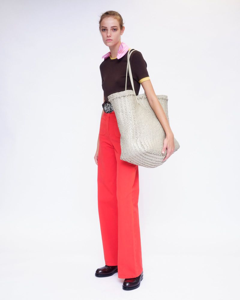 Model wearing a dark brown t-shirt and vibrant red trousers carrying a large woven tote bag against a white backdrop.