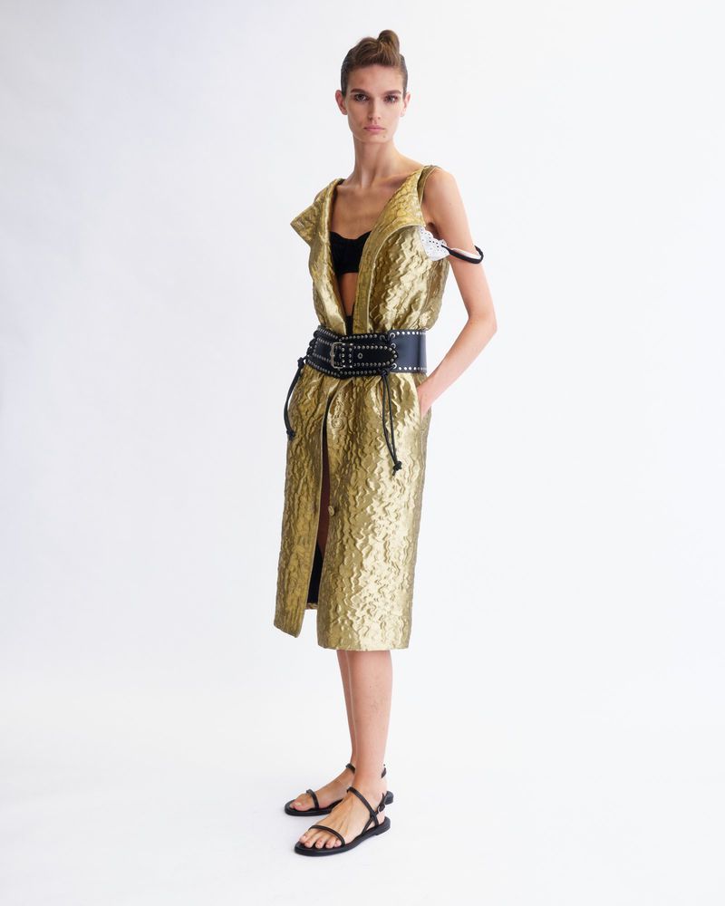 Model wearing a gold textured sleeveless dress with a wide black studded belt against a plain white background.