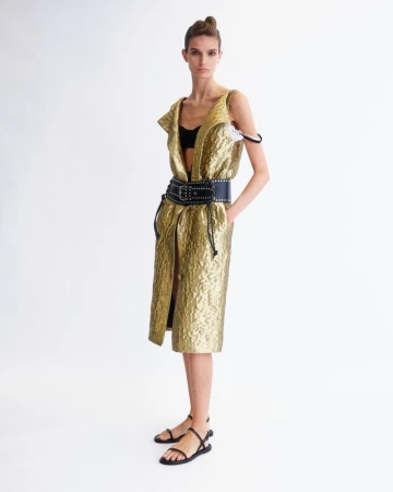 Model wearing a gold textured sleeveless dress with a wide black studded belt against a plain white background.