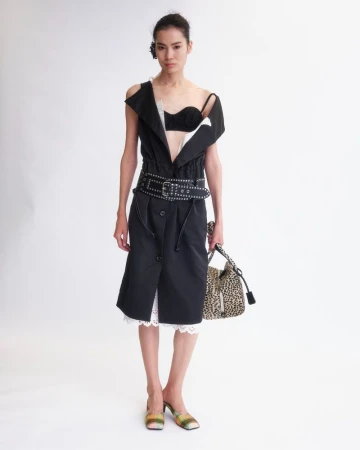 Model in black dress with studded belt and leopard print handbag against a white studio background