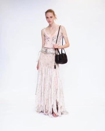 Model wearing a light pink floral dress and wide embellished belt while carrying a dark handbag against a white backdrop.