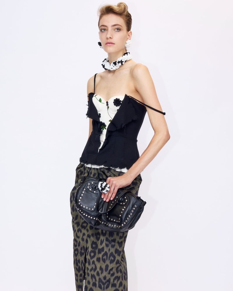 Model wearing a black and white floral top, leopard print skirt, and studded black handbag against a white background