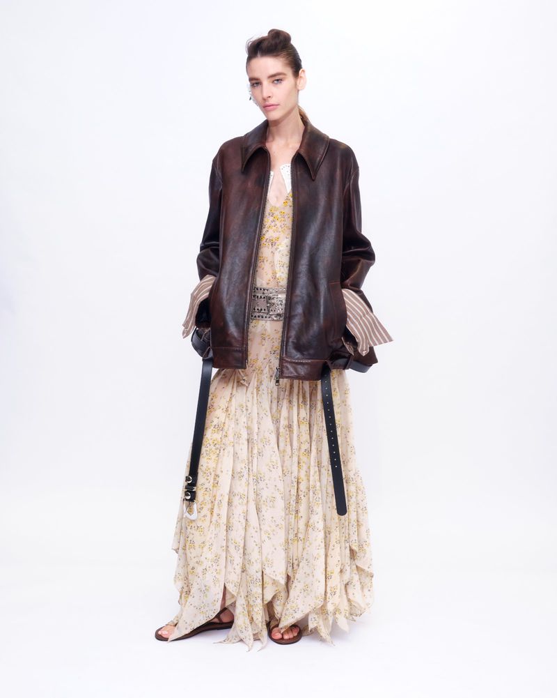 Model wearing a brown leather jacket and patterned dress against a white background for Altuzarra S/S 27