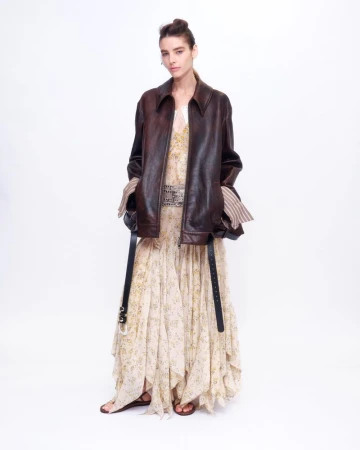 Model wearing a brown leather jacket and patterned dress against a white background for Altuzarra S/S 27