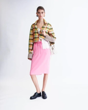 Model wearing a plaid jacket and pink skirt against a white background