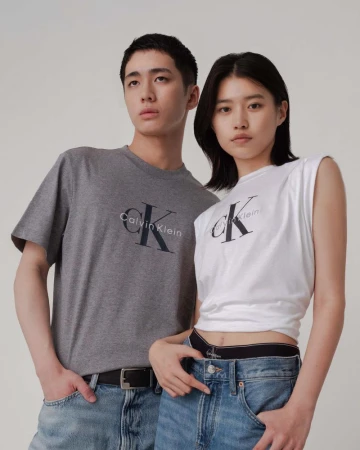 Two models wearing Calvin Klein branded t-shirts and blue jeans against a light grey background