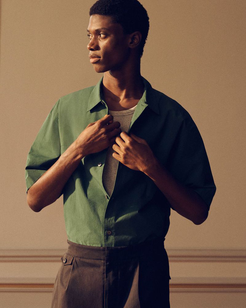Model wearing a green short-sleeve button-down shirt over a light t-shirt against a plain studio background.