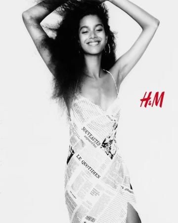 Model wearing a newspaper print dress with arms raised against a white background with H&M logo