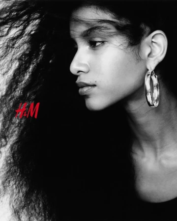 Black and white portrait of a woman with long dark wavy hair wearing large silver hoop earrings.