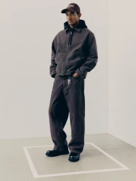 Man wearing a brown denim jacket, matching trousers, and a cap in a clean studio setting