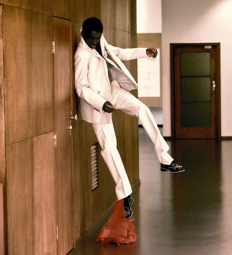 Model Alton Mason in a white suit leaning against wood paneling for Elle Men Brasil, photographed by Lufre.