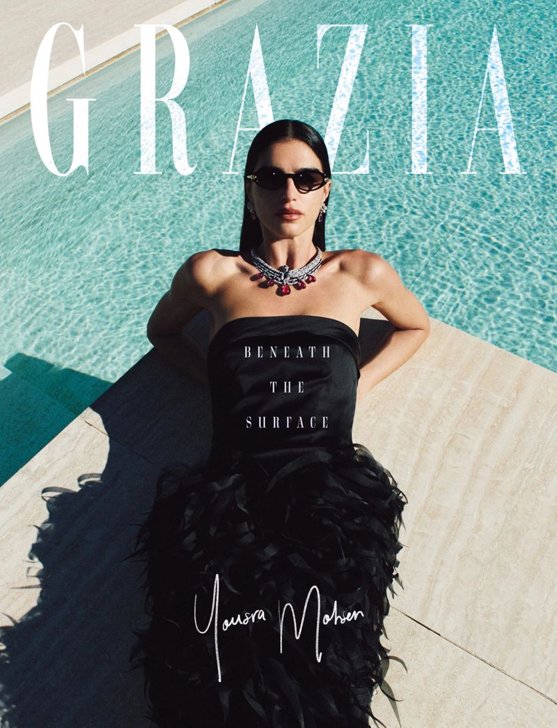 Woman in a black strapless dress and statement necklace posing by an outdoor swimming pool for Grazia Middle East.