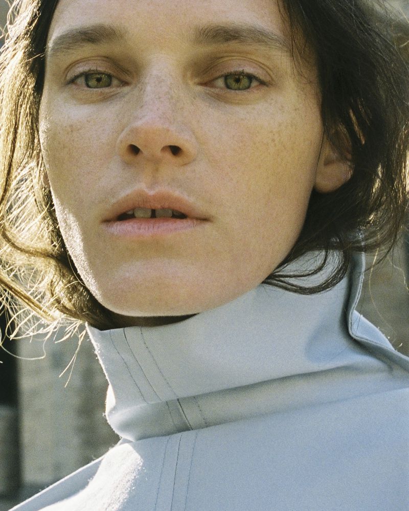 Close-up portrait of a woman with freckles wearing a light blue high collar garment outdoors in sunlight