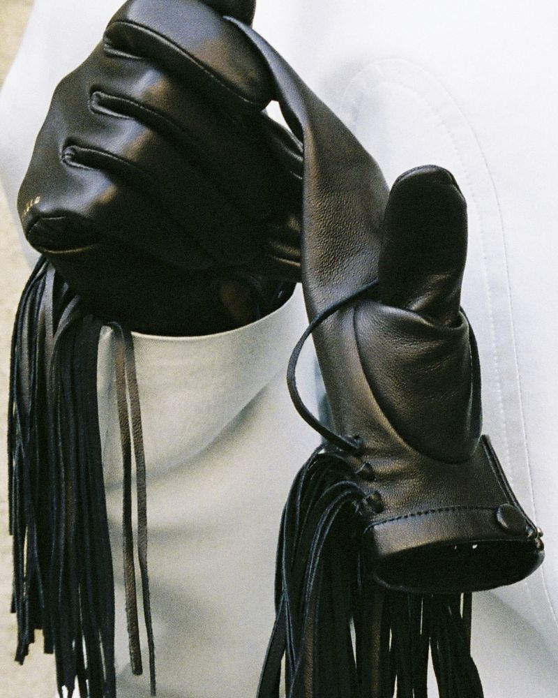 Close-up of black leather gloves with fringe details against a white background for Carven FW26/27.