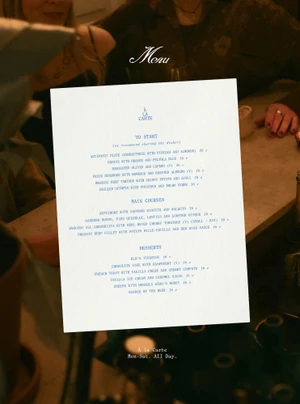 White restaurant menu card displayed centrally over a dim atmospheric table setting with blurred people