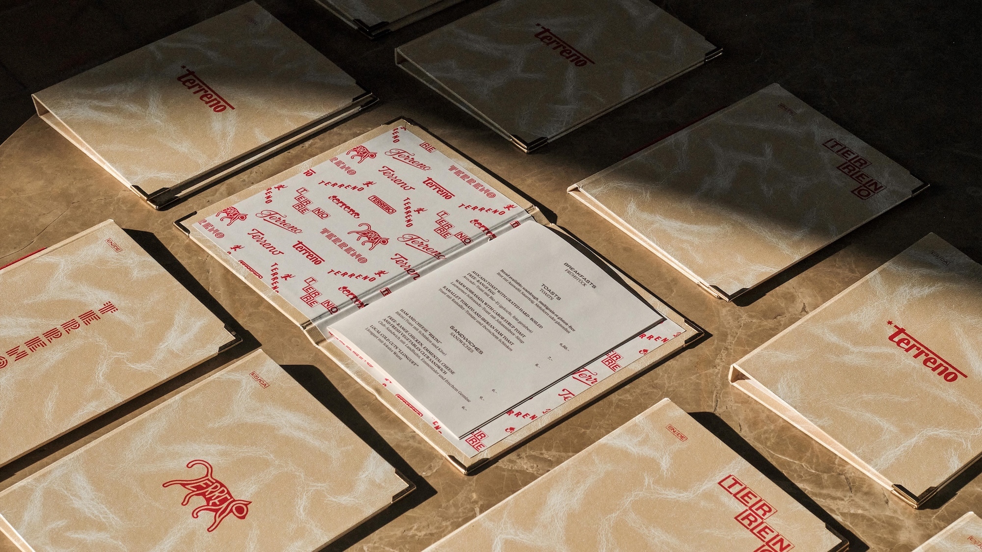 Top-down view of multiple branded menus and binders with red typography on beige textured paper arranged on a dark surface.