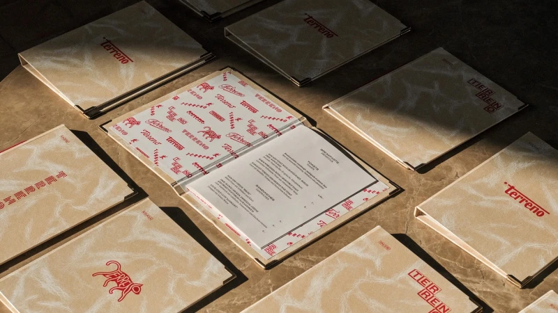 Top-down view of multiple branded menus and binders with red typography on beige textured paper arranged on a dark surface.