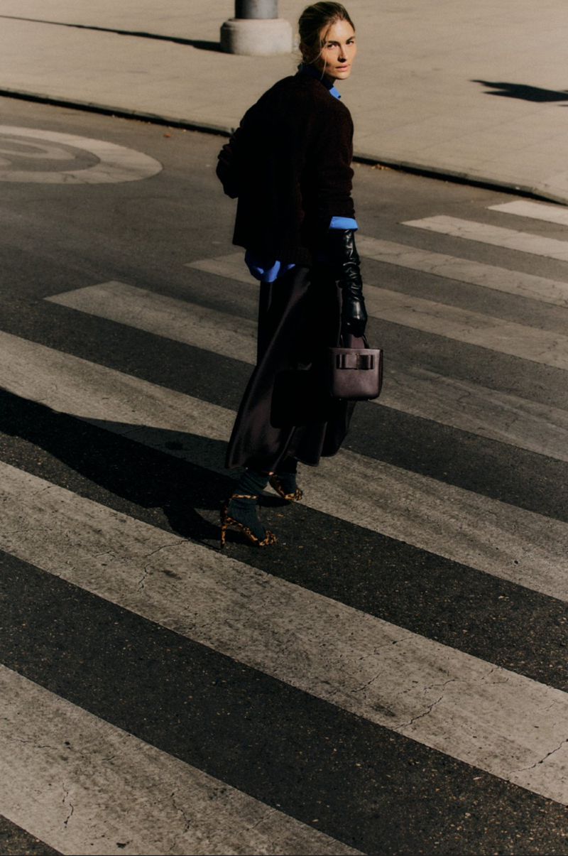 Model Grace Elizabeth crossing a city street carrying a structured leather handbag for Carolina Herrera