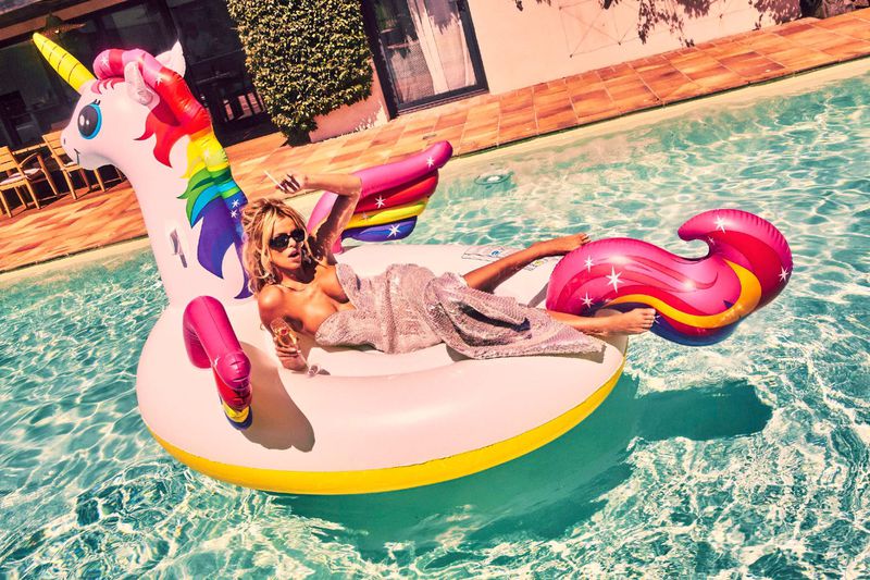 Model Brooks Nader lounging on a giant inflatable unicorn float in an outdoor swimming pool for Von Magazine