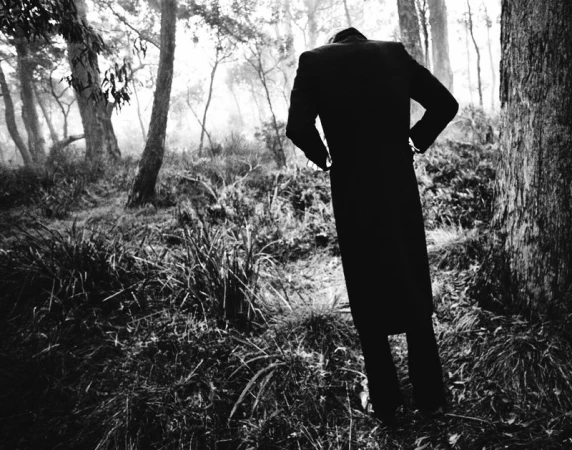 Monochrome image of a person in a long dark coat standing in a misty forest