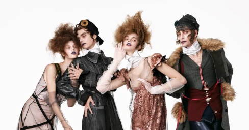 Group of four models in avant-garde styled attire and dramatic hairstyles posing against a solid white background.