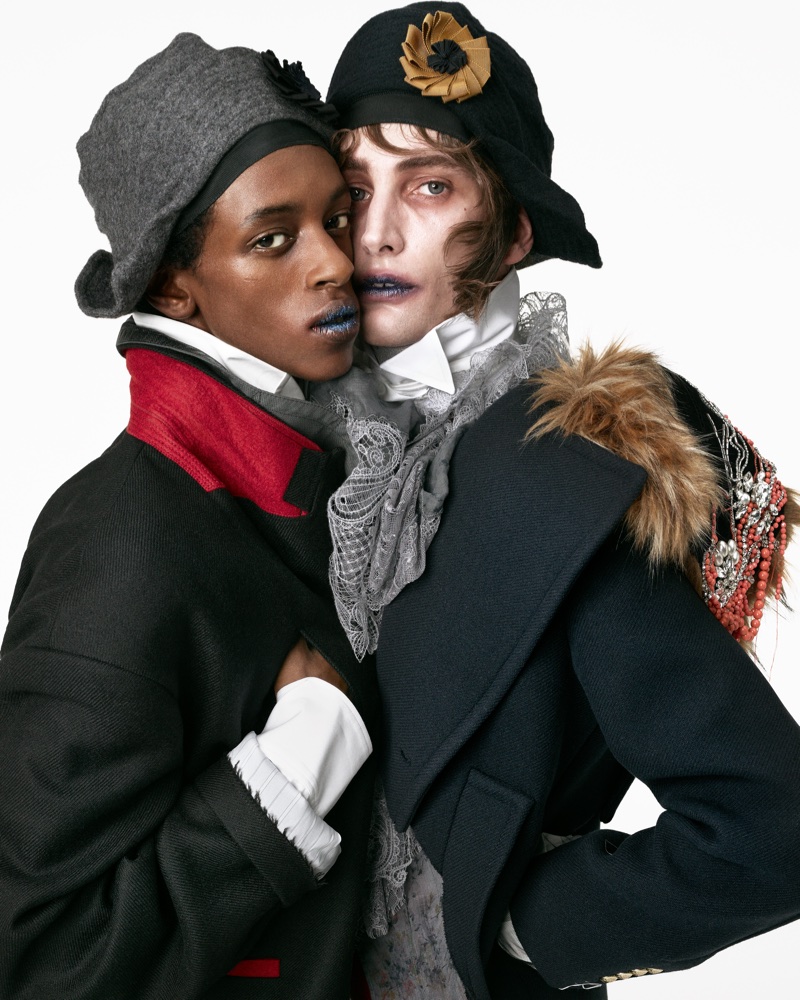 Two models wearing dark coats and cloche hats posing together against a plain white background.