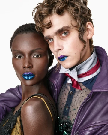 Close-up portrait of two models wearing sparkly blue lipstick and textured apparel against a plain white background