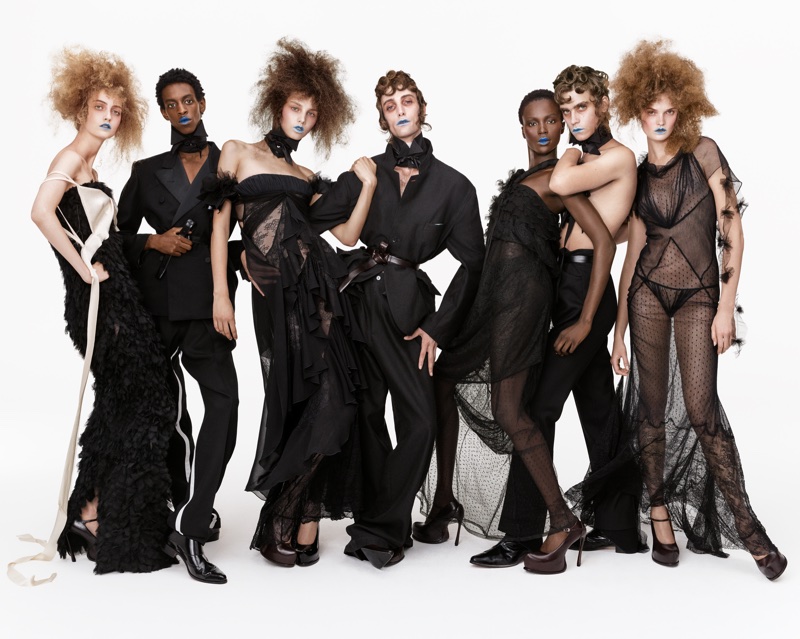 Group of seven models wearing avant-garde black attire and blue lipstick against a clean white background.
