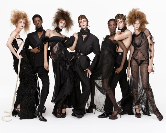 Group of seven models wearing avant-garde black attire and blue lipstick against a clean white background.
